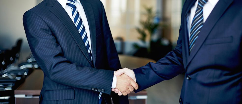 Two businessmen in navy blue suits shaking hands